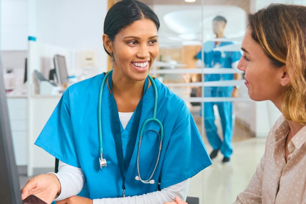 female doctor wearing scrubs at hospital appointment with woman patient looking at digital tablet