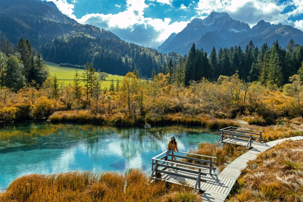 woman sitting on wooden deck by idyllic lake surrounded by idyllic nature in autumn.